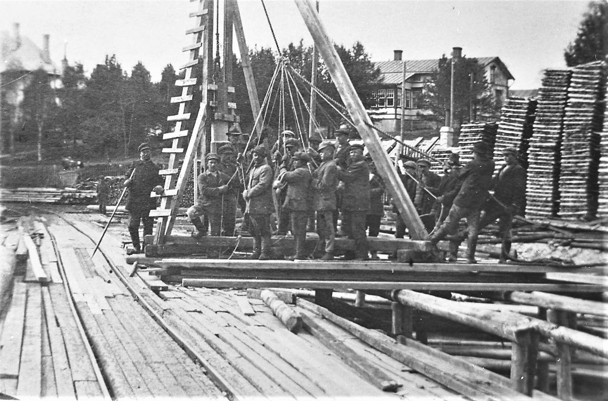 Punainen silta ylitti Äänekosken koskiuoman viistosti lounainen-koillinen suunnassa. Siltaa käytettiin tehtaan sisäisessä junaliikenteessä. Se oli myös suosittu kulkuväylä Hiskinmäen ja keskustan välillä ennen Äänekoski-Suolahti maantiesillan valmistumista vuonna 1950. Kuvassa Punaisen sillan paalutusta oletettavasti sen rakennusvaiheessa 1900-luvun alussa. Taustalla höyryvoimalaitoksen halkopinoja. Halkoja tuotiin suurilla höyrylaivan vetämillä proomuilla pitkin Keitelettä. Naiset pinosivat halot korkeiksi pinoiksi virran länsirannalle, josta ne vietiin hevosen vetämillä kärryillä voimalaitokseen poltettavaksi.