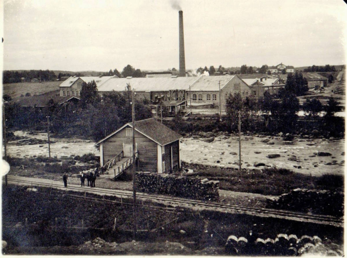 Tehdasaluetta ennen vuotta 1926. Kuvassa etualalla oleva puinen rakennus oli hollikunnan mylly. Tehtaan vesikanavan oikealla reunalla oleva rakennus toimi ainakin välillä uimakoppina ja joissakin vanhoissa kuvissa rakennusta käytettiin mm. uimahyppyesityksiin. Virran takana eli kosken länsipuolella näkyy kartonkitehtaan ja voimalaitoksen rakennuksia ja sen oikella puolella tehtaan pääkonttori. Aivan kuvan oikeassa reunassa näkyy Eerolan talon peltojen läpi kulkeva Kuhnamon pässinrata ja siitä vasemmalle iso ja vaalea rakennus on Eerolan talo, jota isännöivät Honkoset.