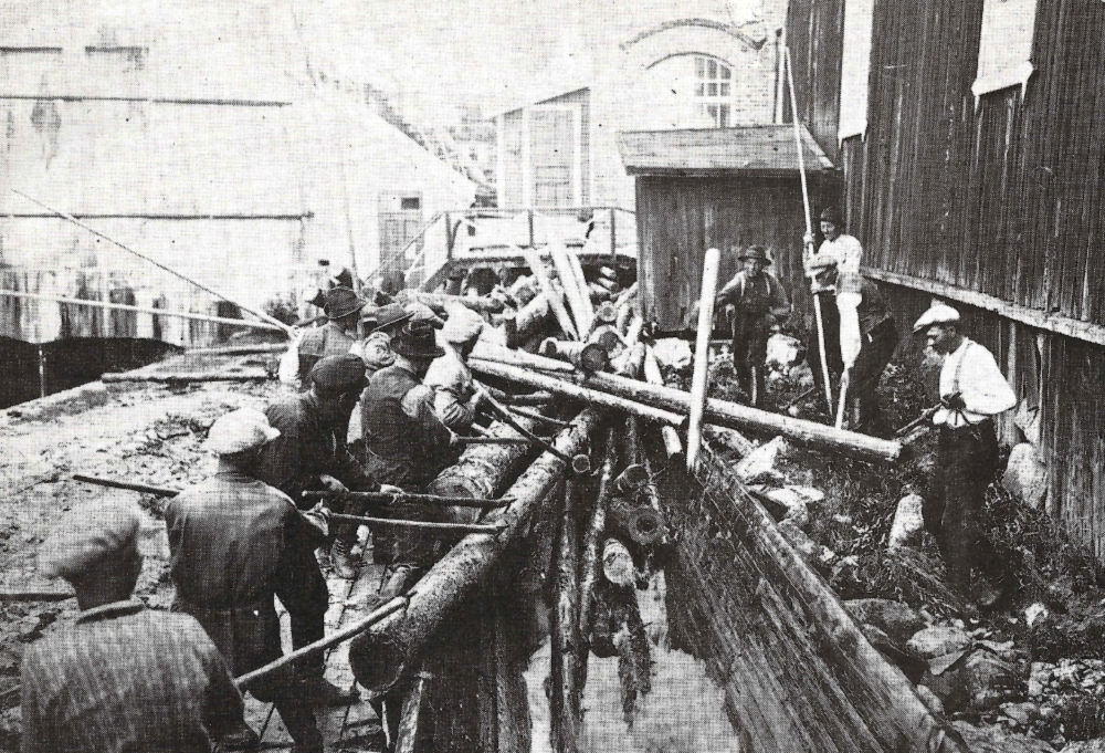 Miehiä purkamassa tukkisumaa Äänekosken tehdasalueen uittorännissä vanhan kartonkikonehallin vierellä 1920-luvun keskivaiheilla. Ränniä pitkin uitettiin Keiteleen puut ohi tehtaan voimalaitoksen. Tukkiränni kulki osan matkaa voimalaitoskanavan alla. Kosken alapuolella etelään menevät puut oli jälleen niputettava lautoiksi.