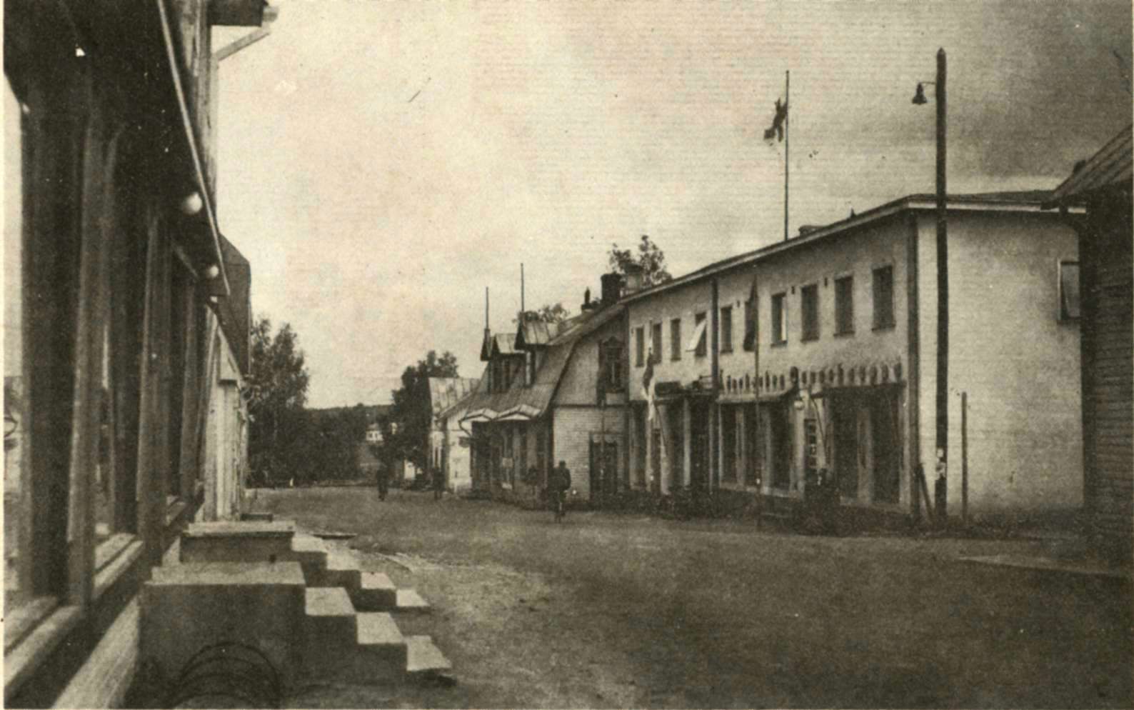 Äänekosken keskustaa vuoden 1936 aikoihin. Tien vasemmalla puolella on meijeri ja Keskimaan myymälä. Kaukana horisontissa häämöttää vaalea Eerolan talo. Tien oikealle puolelle sijoittuvat Kummun Maijan kahvila, Kuutin kahvila. Komeassa puutalossa on myös mm. Äänekosken Osuuskaupan sekatavaraosasto, kivitalossa mm. ruoka- ja jalkineosastot sekä yläkerrassa ravintola.