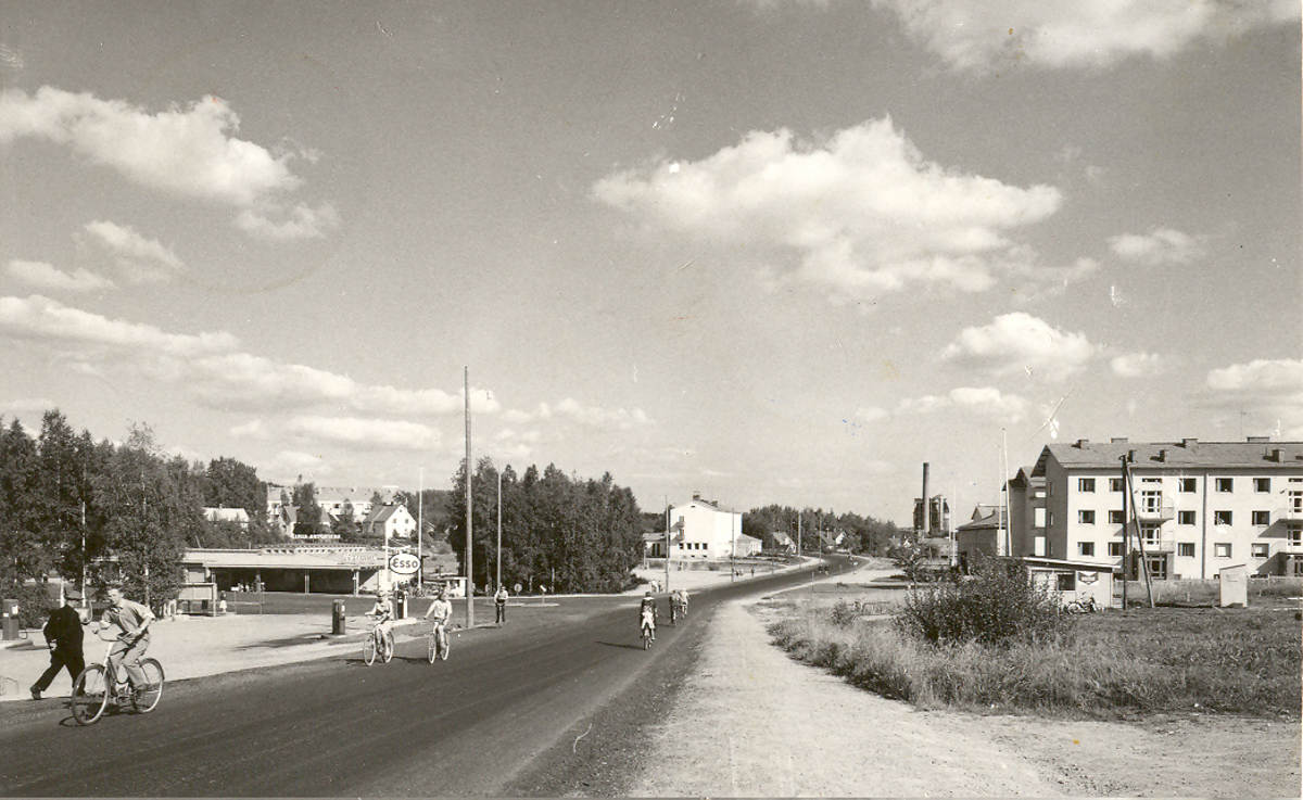 Äänekosken Kotakennääntietä entisen Matkahuollon lähettyviltä vuonna 1961. Paikkakunnan maamerkit happotorni ja vanhan voimalaitoksen savupiippu olivat tuolloin vielä pystyssä. Kuvassa keskellä oleva postitalo oli rakennettu 1952 ja oikeassa reunassa olevat kerrostalot myöskin 1950-luvun aikana. Hirven hotelli, linja-autojen huoltotilat ja tallit, jotka jäävät kuvan vasemman reunan taakse, valmistuivat 1939. Matkahuollon rakennus eli lättähattu purettiin uuden S-marketin tieltä keväällä 2008. Matkahuollon kohdalla oli ennen soinen ryteikkö, jonka kautta kulkivat pitkospuut Pukkimäeltä työväentalolle päin. Alue siistiytyi, kun kauppalan rautatiepysäkki ja linja-autoasema valmistuivat 1950-luvun puolivälissä