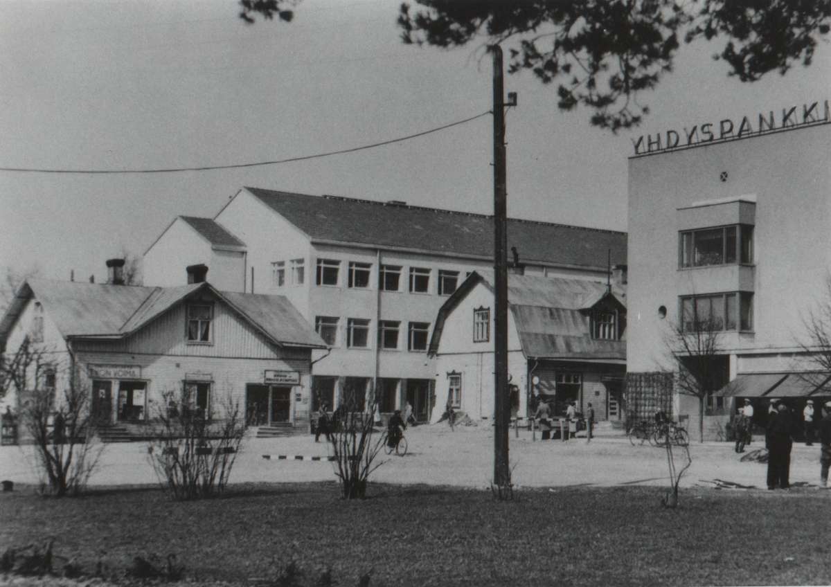 Vuodelta 1952 olevassa kuvassa vasemmalla on Kuutin kahvila, sitten uusi ja vanha osuuskauppa sekä Yhdyspankki. Puinen osuuskaupan rakennus oli entinen Elovaaran kauppatalo, jonka osuuskauppa oli ostanut tehtaan läheltä muutettuaan. Toisessa osuuskaupan rakennuksessa oli ravintola, joka kulki lempinimellä Osula tai Polsu. Talojen välissä kadun varrella oli vanhanaikainen bensanjakelutankki. Osuuskaupan uudemman talon päädyn takaa meni kuja Puuran matkustajakotiin. Yhdyspankin talo valmistui talvisodan alla 1939. Rakennuksen katutasossa oli erikokoisia liikehuoneistoja ja sen eteläpuolella pankin pääoven vieressä oli Alkon myymälä. Vanhat, puiset rakennukset purettiin melko pian kuvan ottamisen jälkeen.