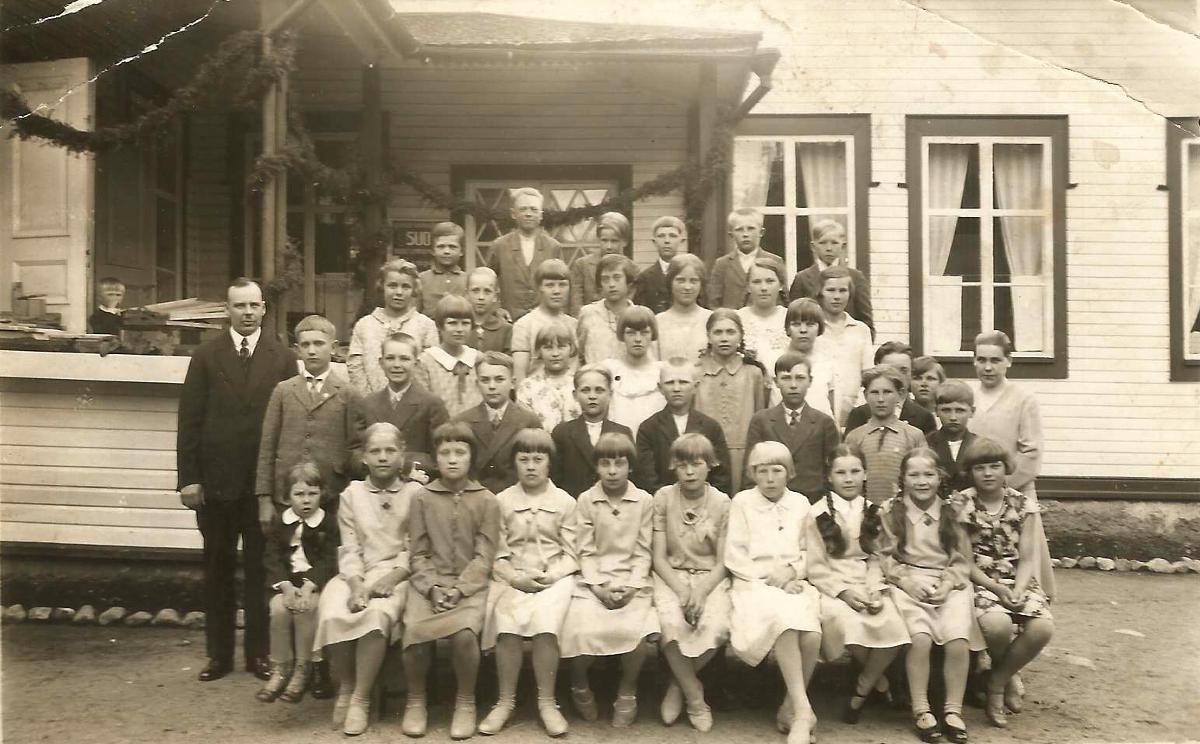 Piilolanniemen kansakoulun oppilaita ja opettaja ehkä vuonna 1930. Kuvassa vasemmalla opettaja J.A. Leppämäki. Kuka on oikealla oleva naisopettaja? Tunnistaako joku joitakin oppilaita kuvasta?