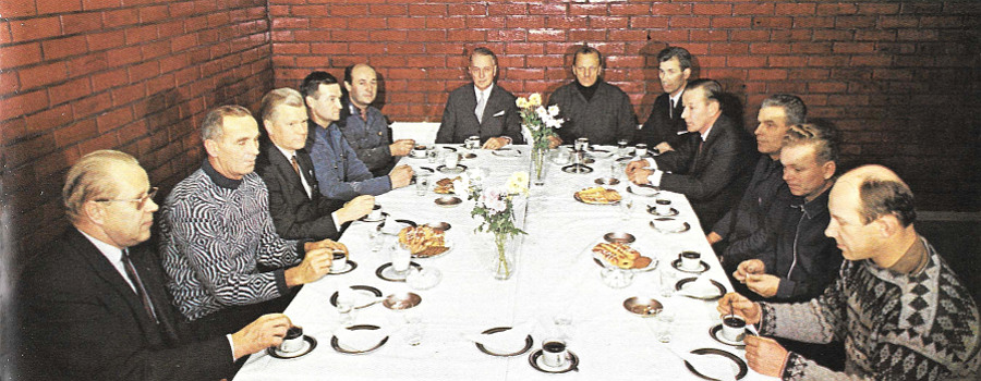 Kahvihetki tehtaiden työmaaruokalassa. Pöydän päässä oikealla tehtaiden tuotantokomitean puheenjohtaja koneenhoitaja Eino Rahkonen ja hänen vieressään yhtiön toimitusjohtaja vuorineuvos Wolter Westerholm. Heidän lisäkseen kuvassa ovat alkaen vasemmalta: Tehtaiden sosiaalipäällikkö Leo Töllikkö sekä tuotantokomitean jäsenet kuivaamonhoitaja Reino Nieminen, teknikko Lauri Pajari, sähköylimestari Matti Kekki, laitosmies Valter Melasalmi, dipl.ins. Erkki Aalto, agronomi Toivo Ora, työnjohtaja Väinö Ahvenainen, valkaisija Matti Kalenius ja äärimmäisenä oikealla tehtaiden pääluottamusmies Martti Pöyhönen.