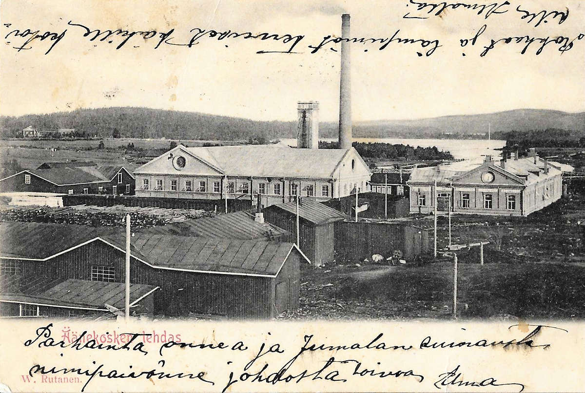 Äänekosken tehtaat aivan 1900-luvun taitteessa. Vasemmalla kartonkitehdas, voimalaitos ja hiomo. Korkean savipiipun vasemmalla puolella on käsin tehtyjen arkkien kuivaukseen käytetty 30 metriä korkea kuivauskanaali. Kuvaukseen menevät arkit ripustettiin silloin käsin vaunuun, jolla ne siirrettiin kuivauskanaaliin sisälle. Kuivuneet arkit poistettiin myöhemmin kanaalista vaunun avulla ja pakattiin maailmalle lähettämistä varten. Kuivauskanaali purettiin myöhemmin voimalaitoksen laajennuksen tieltä 1920-luvulla. Oikealla konttorirakennus vartiokoppeineen. Kuva on otettu ennen vuotta 1906 eli aikaan ennen paperikoneen rakentamista Äänekoskelle. Kartonkituotannon määrä 1900-luvun alussa vaihteli paljon, mutta oli kokoluokaltaan kuitenkin huomattavasti alle 5000 tn vuosi.