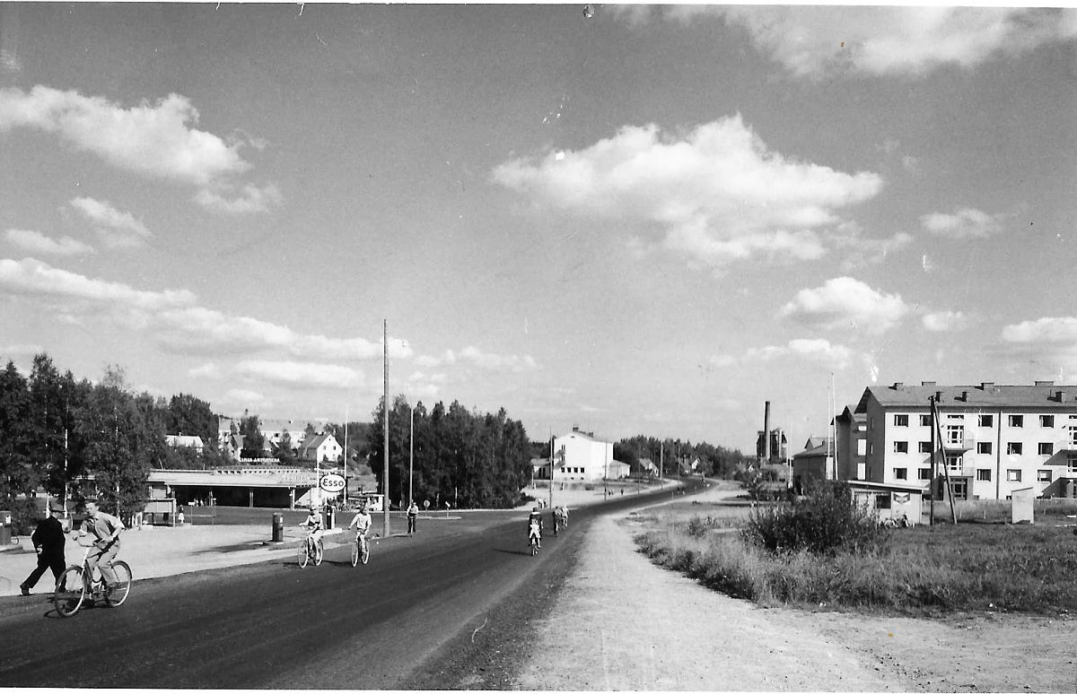 Äänekosken Kotakennääntietä entisen Matkahuollon lähettyviltä vuonna 1961. Paikkakunnan maamerkit happotorni ja vanhan voimalaitoksen savupiippu olivat tuolloin vielä pystyssä. Kuvassa keskellä oleva postitalo oli rakennettu 1952 ja oikeassa reunassa olevat kerrostalot myöskin 1950-luvun aikana. Hirven hotelli, linja-autojen huoltotilat ja tallit, jotka jäävät kuvan vasemman reunan taakse, valmistuivat 1939. Matkahuollon rakennus eli lättähattu purettiin uuden S-marketin tieltä keväällä 2008. Matkahuollon kohdalla oli ennen soinen ryteikkö, jonka kautta kulkivat pitkospuut Pukkimäeltä työväentalolle päin. Alue siistiytyi, kun kauppalan rautatiepysäkki ja linja-autoasema valmistuivat 1950-luvun puolivälissä