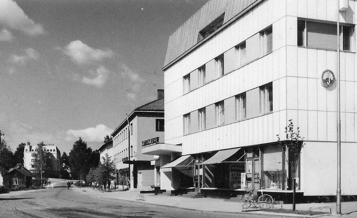Äänekosken keskustan liikerakennuksia. Etualalla Säästöpankin vuonna 1939 valmistunut rakennus, jota on laajennettu ja korotettu myöhemmin. Sen takana Apran eli apteekin ja rautakaupan vuonna 1952 valmistunut rakennus. Niiden välissä oleva KOP:n talo valmistui vuonna 1950. Taustalla vasemmalla vuonna 1961 valmistunut Kauppakatu 22 eli ns. Lompsalinnan rakennus.